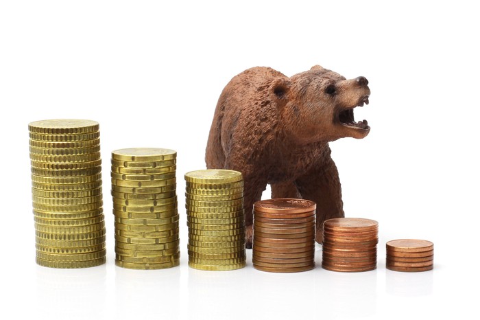 A brown bear stands behind a row of increasingly taller coin piles.