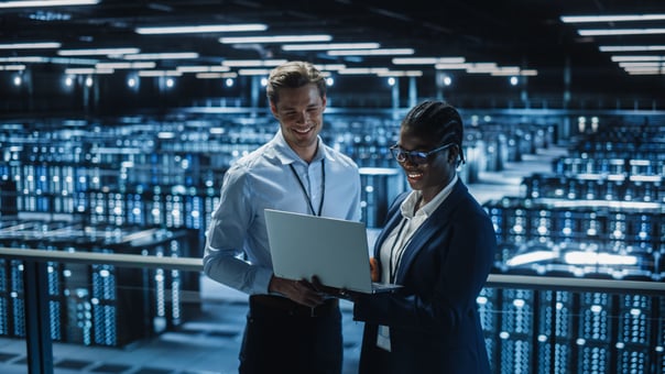 Two smiling employees looking at a laptop computer inside a data center