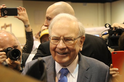 Warren Buffett smiling, surrounded by cameras