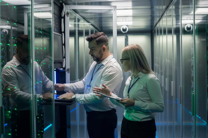 two people stand in a database room looking at a server and discussing the device