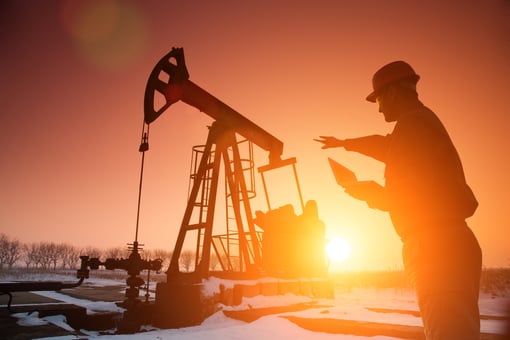 A person working near an oil pump with the sun setting in the background.