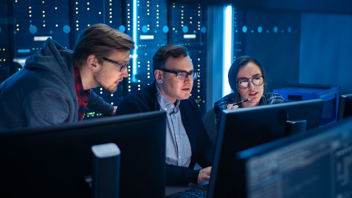 Three people looking at monitors in server room.